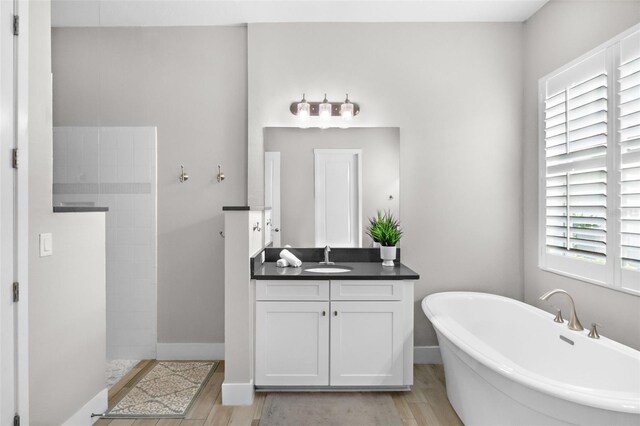 full bath featuring wood finished floors, walk in shower, a freestanding bath, vanity, and baseboards