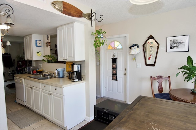 kitchen featuring a textured ceiling, a sink, light tile patterned flooring, white cabinetry, and white dishwasher