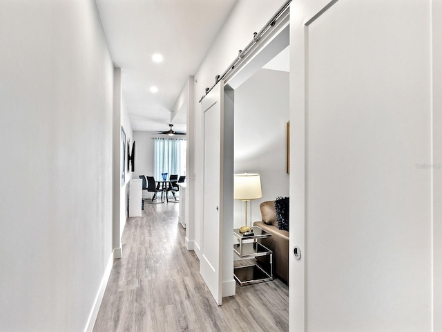corridor with baseboards, recessed lighting, light wood-style floors, and a barn door
