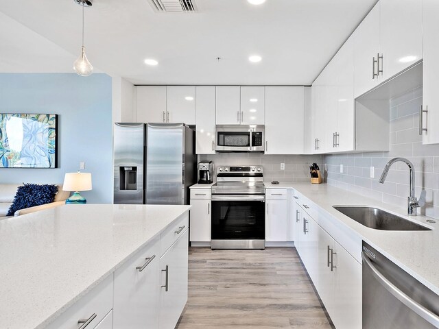kitchen with decorative light fixtures, modern cabinets, a sink, white cabinetry, and stainless steel appliances