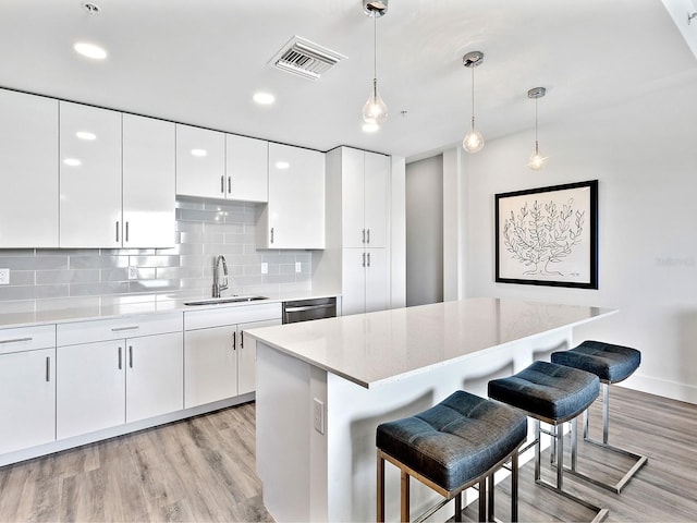 kitchen with a sink, visible vents, light wood finished floors, a kitchen bar, and white cabinets