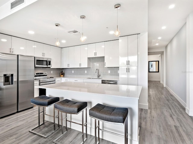 kitchen featuring light wood finished floors, stainless steel appliances, visible vents, and a sink
