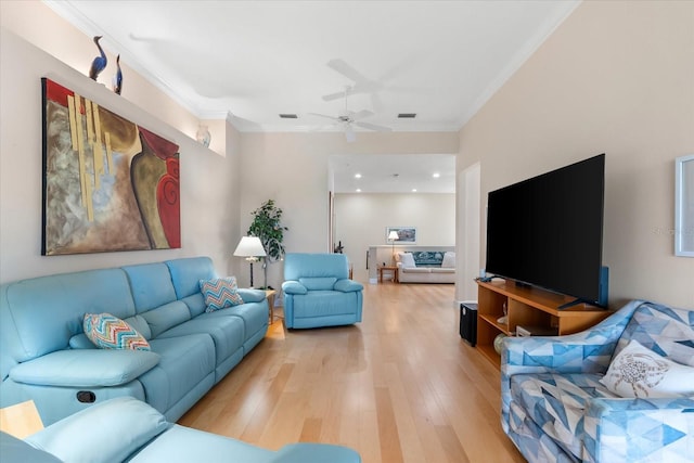 living room featuring ornamental molding, light wood-style flooring, a ceiling fan, and visible vents