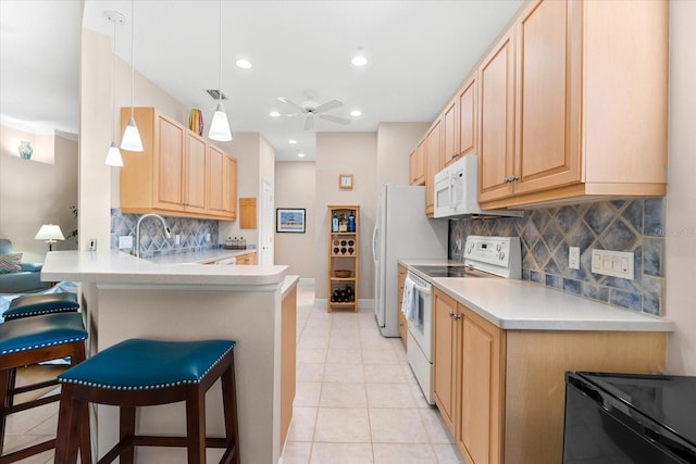 kitchen featuring white appliances, light tile patterned floors, a peninsula, a kitchen bar, and light brown cabinetry