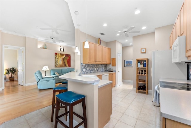 kitchen with white appliances, a peninsula, a ceiling fan, a sink, and light brown cabinets