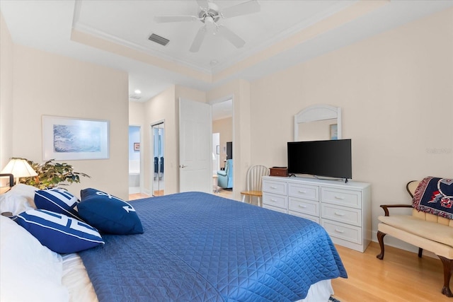 bedroom featuring visible vents, light wood-type flooring, crown molding, a tray ceiling, and ensuite bath
