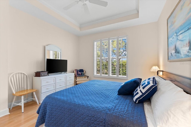 bedroom featuring baseboards, a raised ceiling, crown molding, ceiling fan, and light wood finished floors