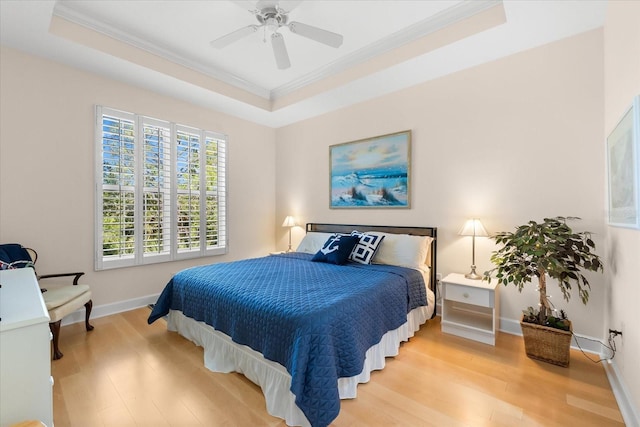 bedroom with baseboards, a ceiling fan, crown molding, a tray ceiling, and wood finished floors