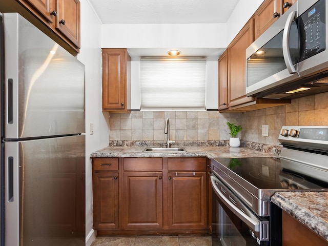 kitchen featuring tasteful backsplash, appliances with stainless steel finishes, a sink, and brown cabinets
