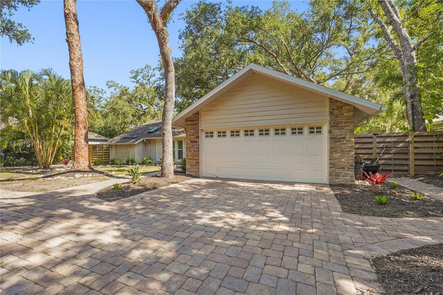 view of front of house featuring decorative driveway, fence, stone siding, and a garage