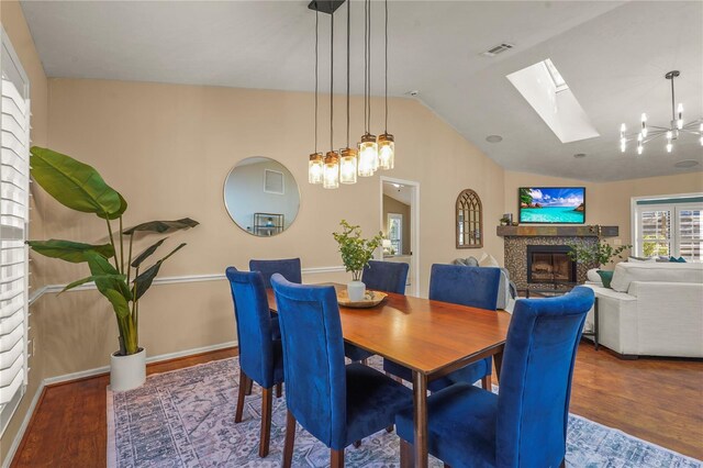 dining room with lofted ceiling with skylight, wood finished floors, a chandelier, and a fireplace