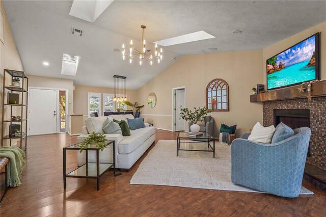 living area featuring visible vents, a fireplace, wood finished floors, lofted ceiling with skylight, and a notable chandelier