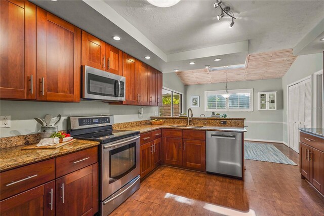 kitchen with a sink, appliances with stainless steel finishes, a peninsula, and dark wood finished floors