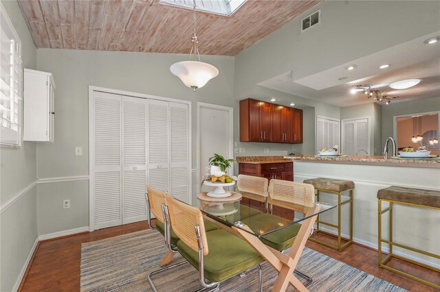 dining area with baseboards, lofted ceiling with skylight, wood finished floors, and visible vents