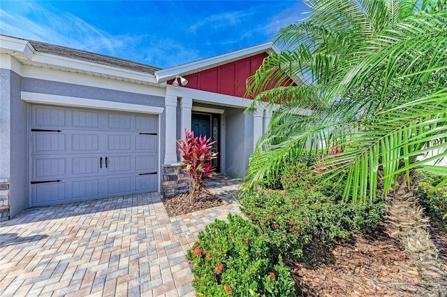 entrance to property featuring stucco siding, stone siding, decorative driveway, and an attached garage