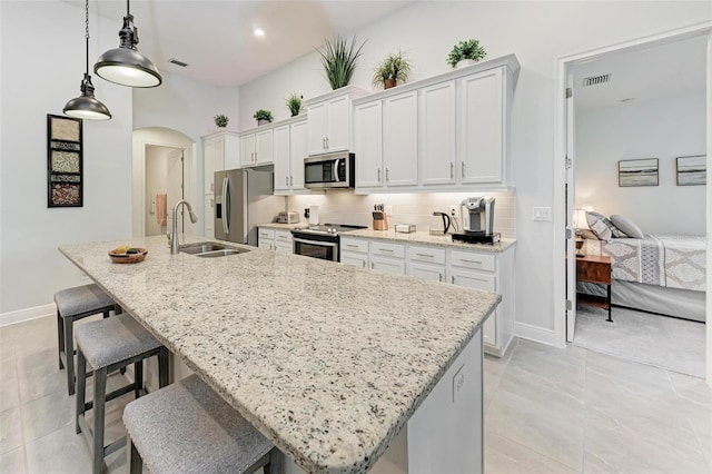 kitchen featuring an island with sink, arched walkways, visible vents, a sink, and stainless steel appliances