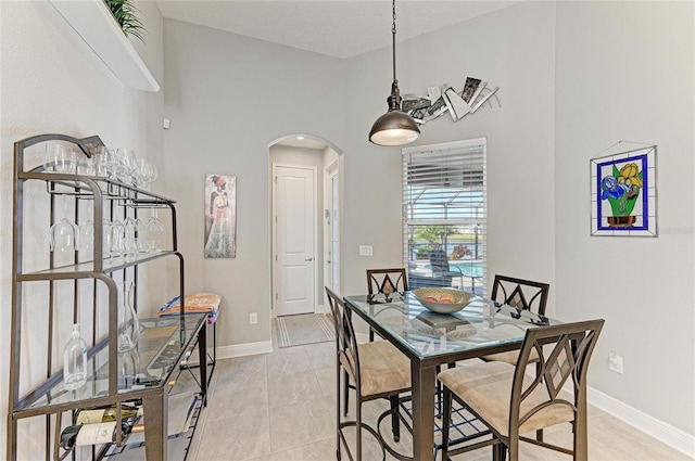 dining room featuring arched walkways, light tile patterned floors, and baseboards