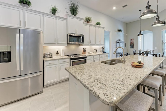 kitchen with a kitchen breakfast bar, appliances with stainless steel finishes, a kitchen island with sink, a sink, and backsplash