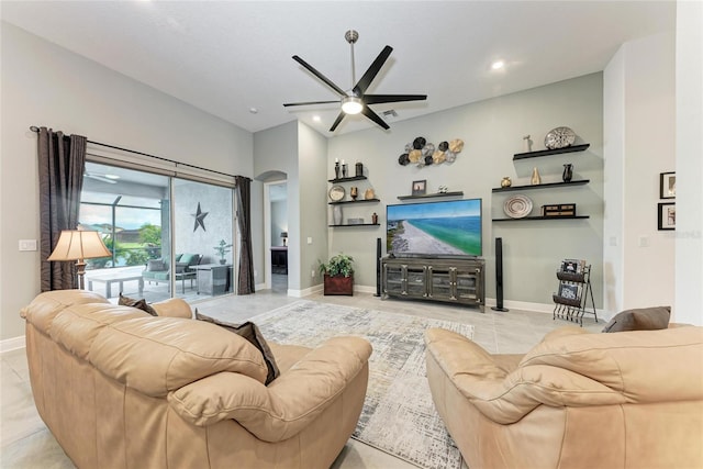 living room featuring arched walkways, light tile patterned floors, baseboards, and a ceiling fan