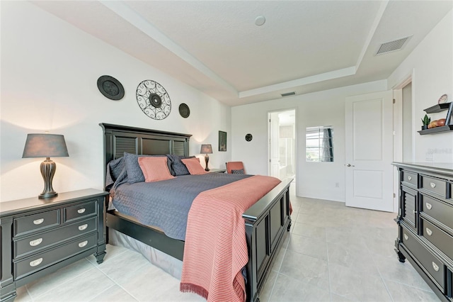 bedroom with a raised ceiling, light tile patterned flooring, visible vents, and connected bathroom