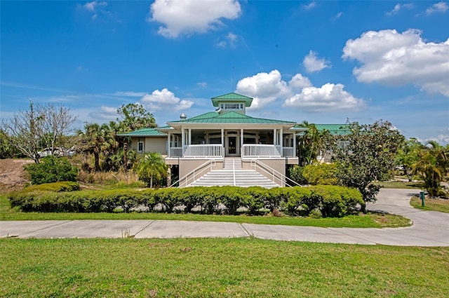 coastal home with a porch, a standing seam roof, metal roof, a front yard, and stairway