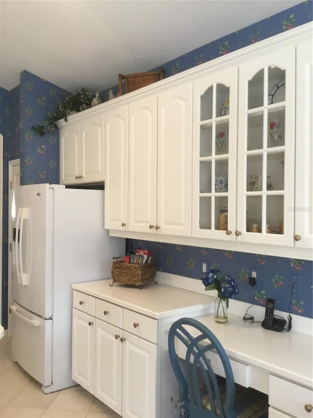 kitchen with light countertops, white cabinets, freestanding refrigerator, glass insert cabinets, and wallpapered walls