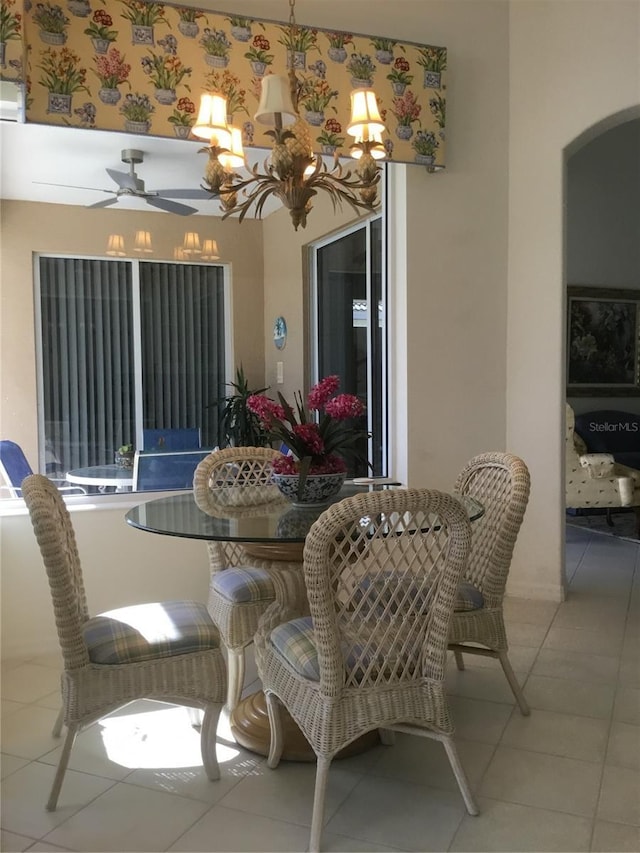 dining area featuring arched walkways, tile patterned floors, and ceiling fan with notable chandelier