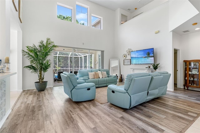 living area with a sunroom, plenty of natural light, wood finished floors, and a towering ceiling