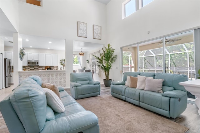 living area with a sunroom, a ceiling fan, light wood finished floors, and a towering ceiling