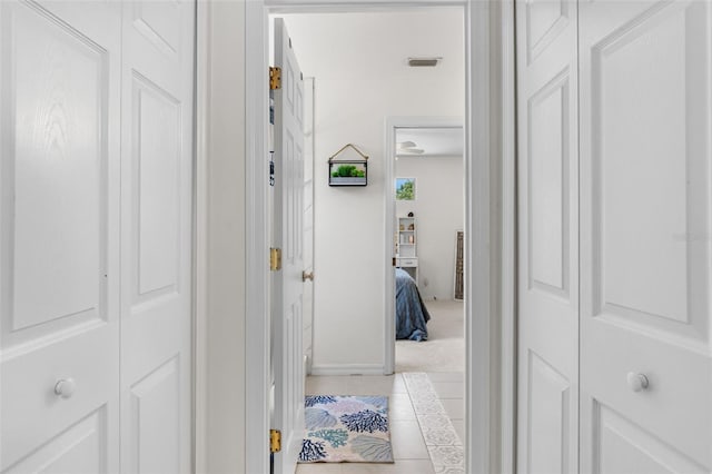 hallway with baseboards, visible vents, and light tile patterned floors