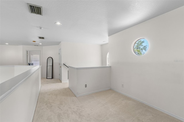 hallway featuring visible vents, light carpet, and an upstairs landing