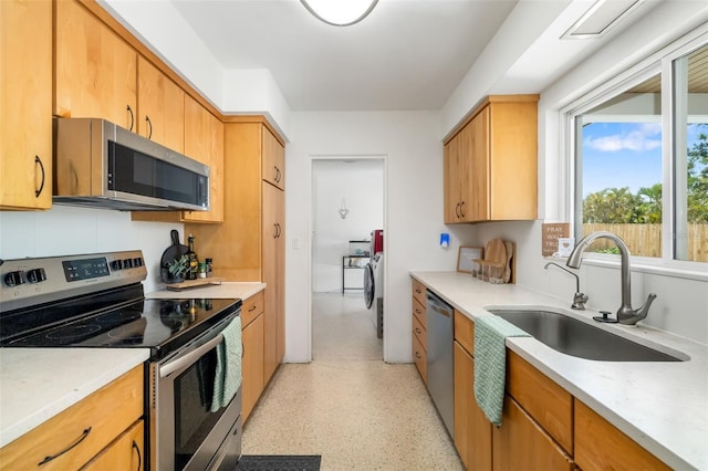 kitchen with washing machine and clothes dryer, appliances with stainless steel finishes, light countertops, and a sink