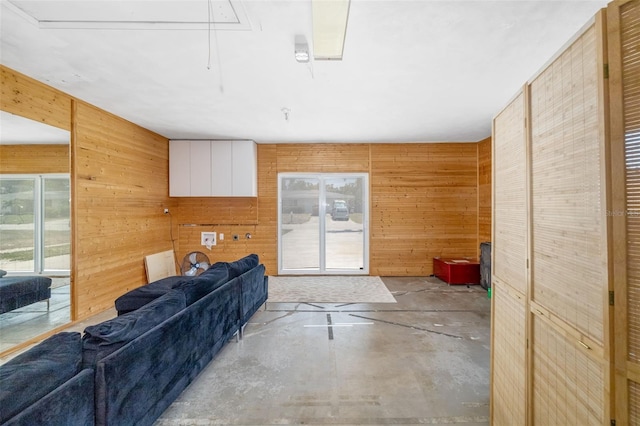 living room with attic access, wooden walls, and concrete flooring