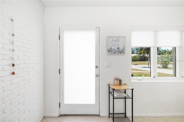 doorway to outside with speckled floor, baseboards, and brick wall
