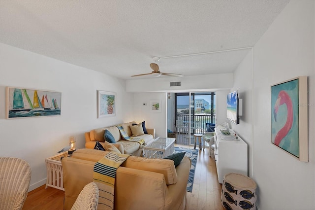living area featuring ceiling fan, visible vents, a textured ceiling, and light wood finished floors