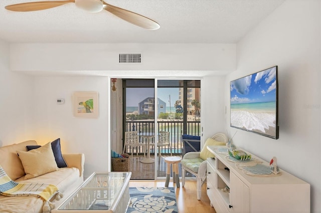living room featuring a textured ceiling, light wood-style flooring, visible vents, and a ceiling fan