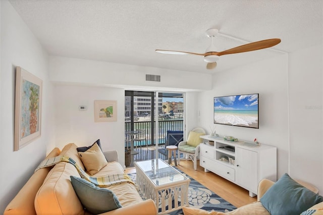 living room with a ceiling fan, a textured ceiling, visible vents, and light wood-style flooring