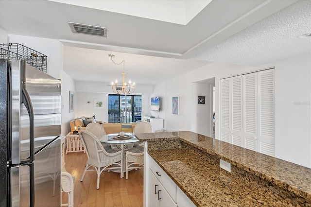 kitchen with a chandelier, light wood-style floors, white cabinetry, visible vents, and freestanding refrigerator