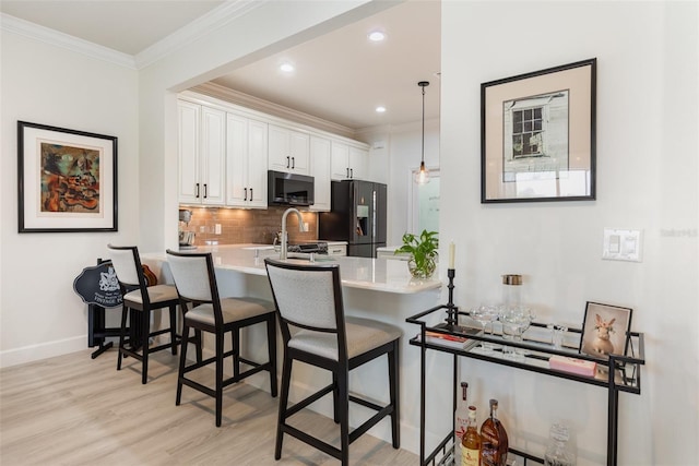 2705 Taheebo Way, North Port, FL 34289 - kitchen featuring black refrigerator with ice dispenser, a peninsula, light wood-style floors, a kitchen bar, and white cabinets
