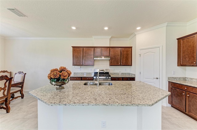 kitchen with stainless steel gas range oven, light stone counters, under cabinet range hood, visible vents, and a sink