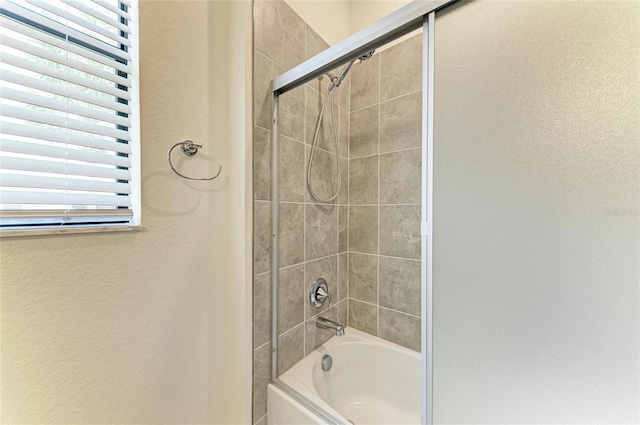 bathroom featuring shower / bath combination with glass door and a textured wall
