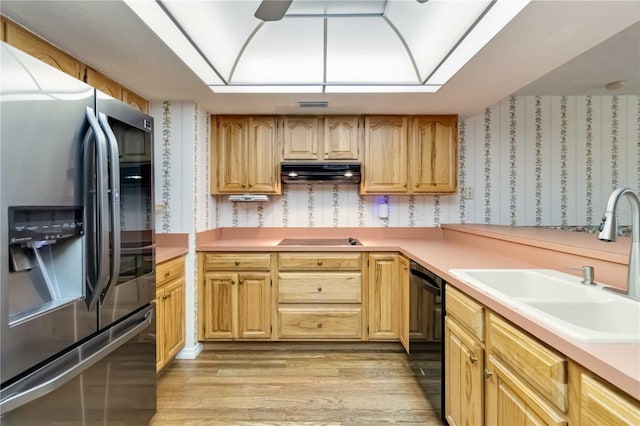 kitchen featuring light wood-style floors, wallpapered walls, under cabinet range hood, a sink, and black appliances
