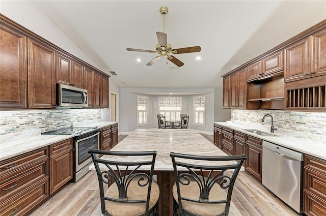 kitchen with open shelves, lofted ceiling, light wood-type flooring, a sink, and stainless steel appliances