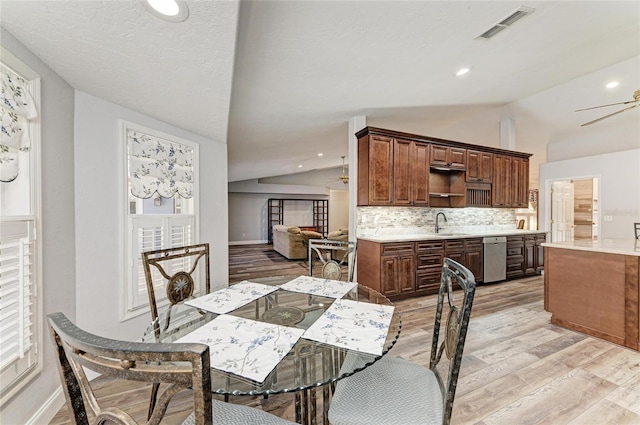 dining room featuring light wood-style floors, vaulted ceiling, and visible vents