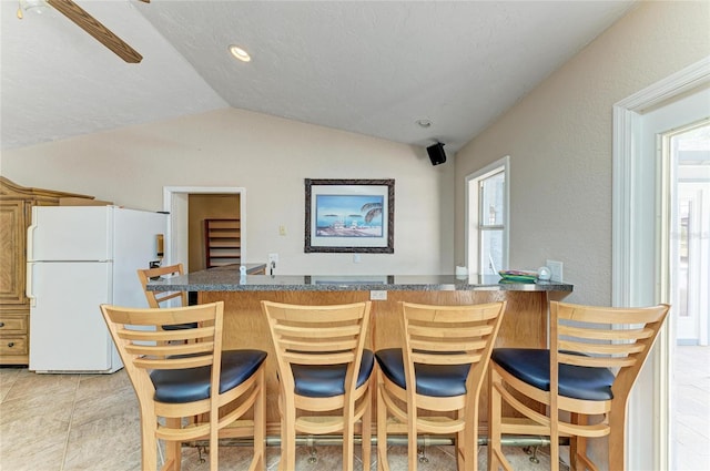 kitchen featuring dark countertops, freestanding refrigerator, a kitchen bar, and lofted ceiling