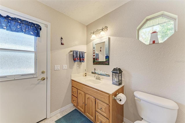 half bathroom featuring toilet, vanity, plenty of natural light, and a textured wall