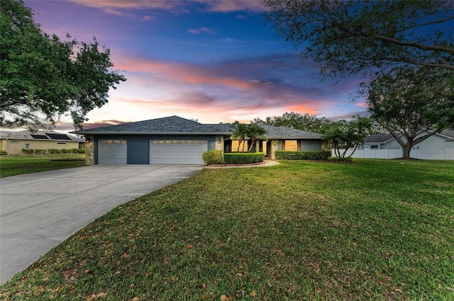 ranch-style home with driveway, fence, a yard, an attached garage, and stucco siding