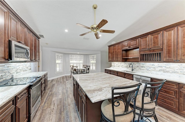 kitchen with a ceiling fan, a sink, open shelves, appliances with stainless steel finishes, and a kitchen island