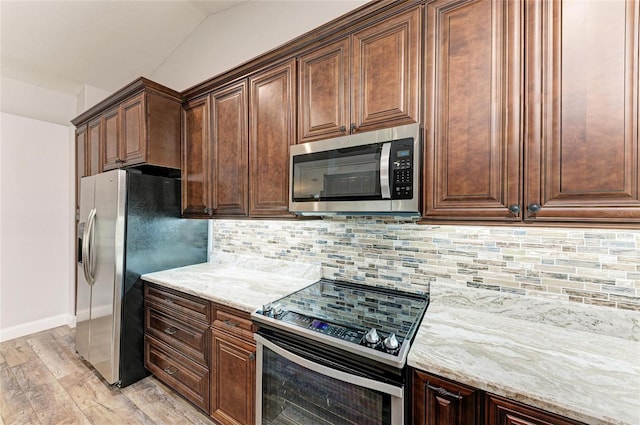 kitchen featuring light wood-style flooring, stainless steel appliances, baseboards, light stone countertops, and decorative backsplash