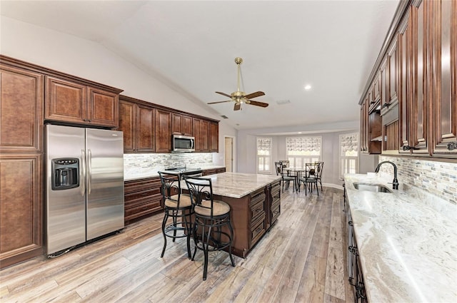 kitchen featuring lofted ceiling, a ceiling fan, light wood finished floors, a sink, and stainless steel appliances